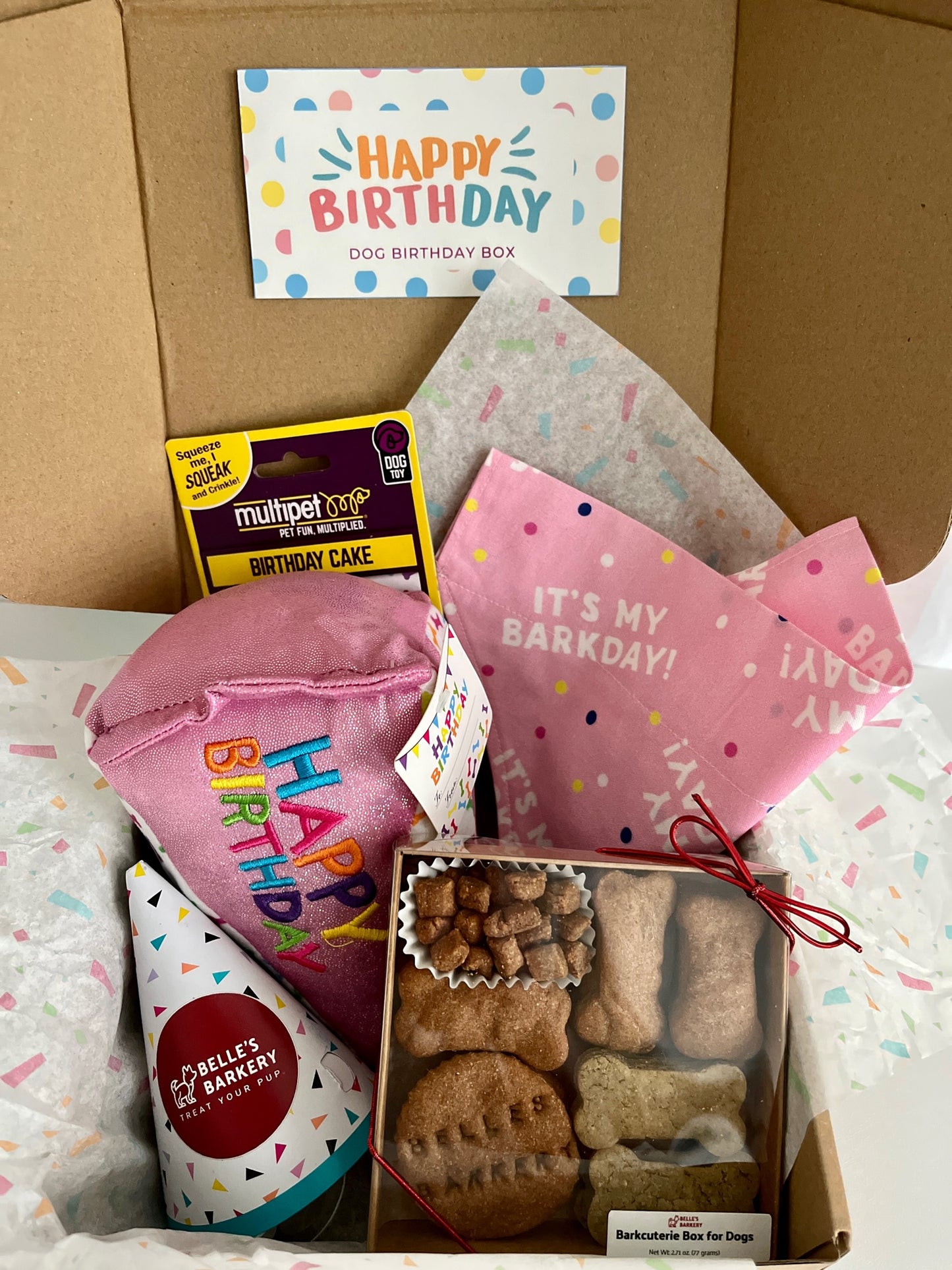 Happy Birthday Box featuring pink dog birthday slice toy, birthday bandana in pink, Belle's Barkery Barkcuterie Box, and birthday hat