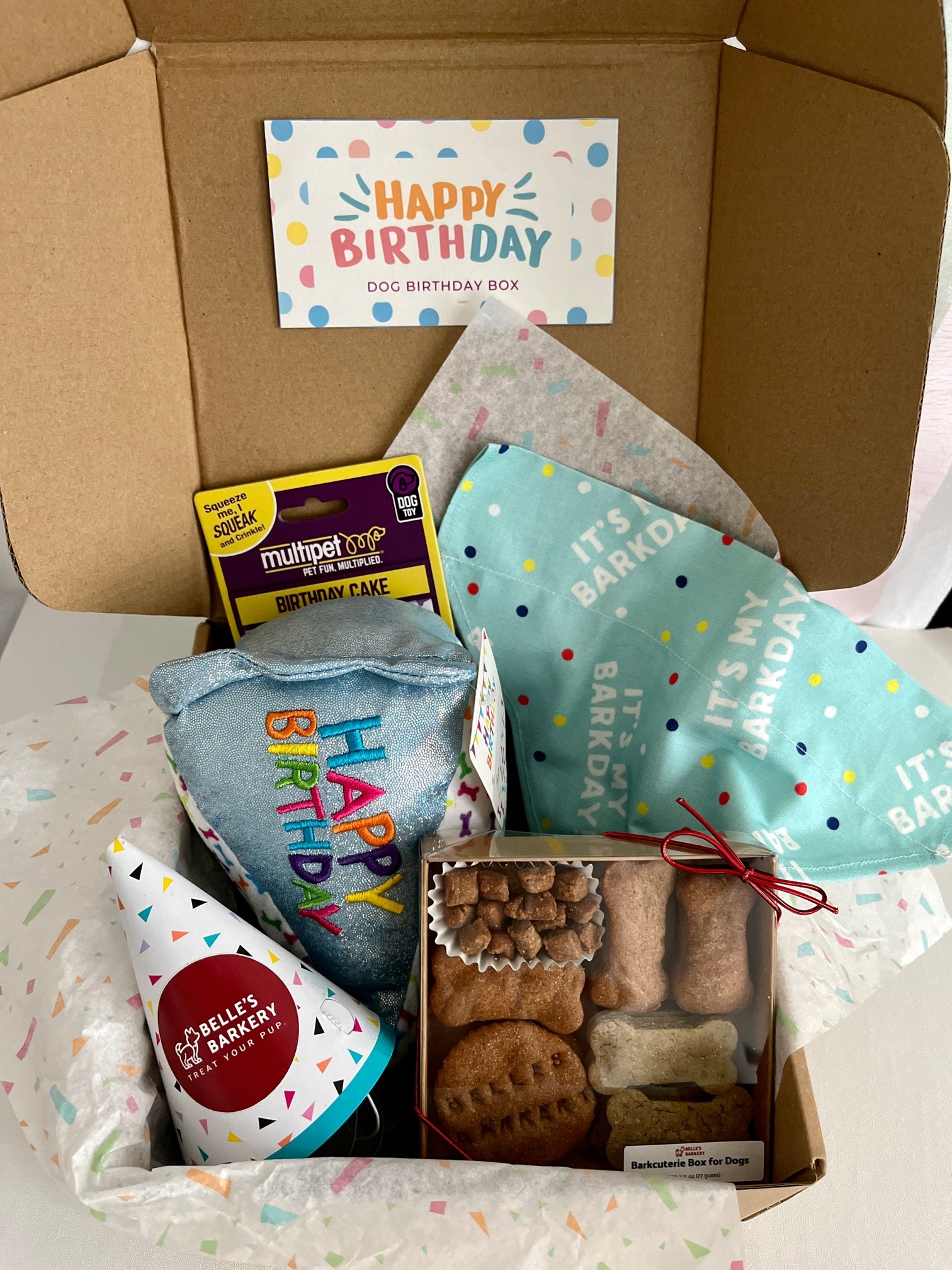 Happy Birthday Box featuring blue dog birthday slice toy, birthday bandana in blue, Belle's Barkery Barkcuterie Box, and birthday hat
