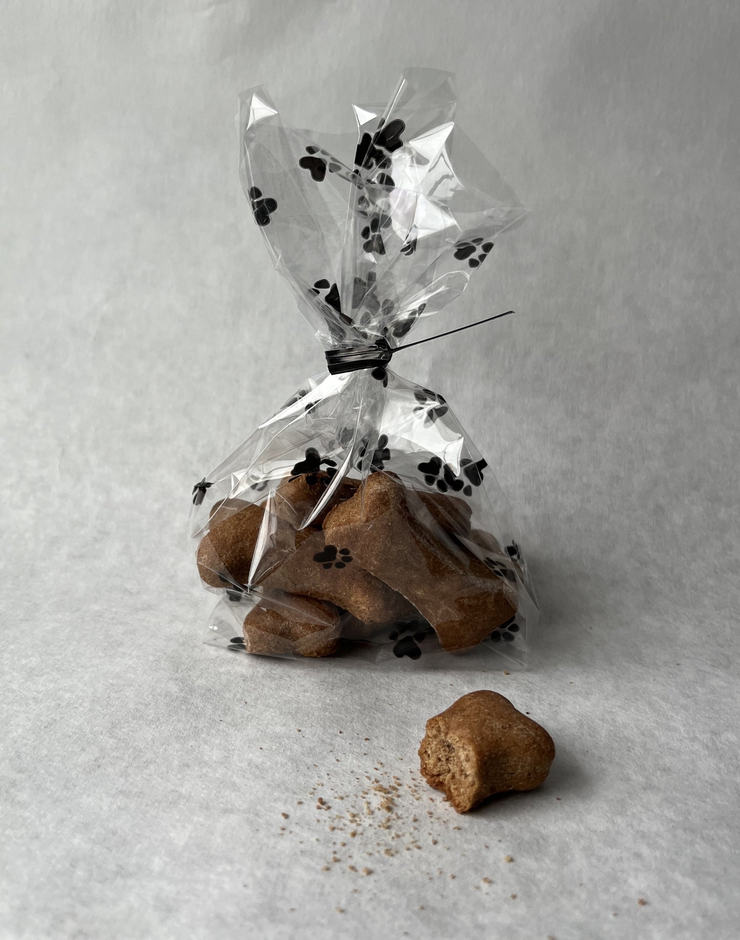 Dog goodie bag filled with baked biscuit dog treats. One dog treat with bite out of it  is shown near the goody bag. 